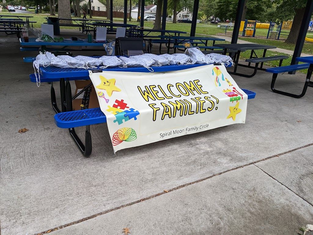 Banner stating "Welcome Families - Spiral Moon Family Circle" with kids toys on each side of the letters. The banner is taped to a picnic table, and the table has goodie bags for kids. Photo taken at Pagan Pride 2022.