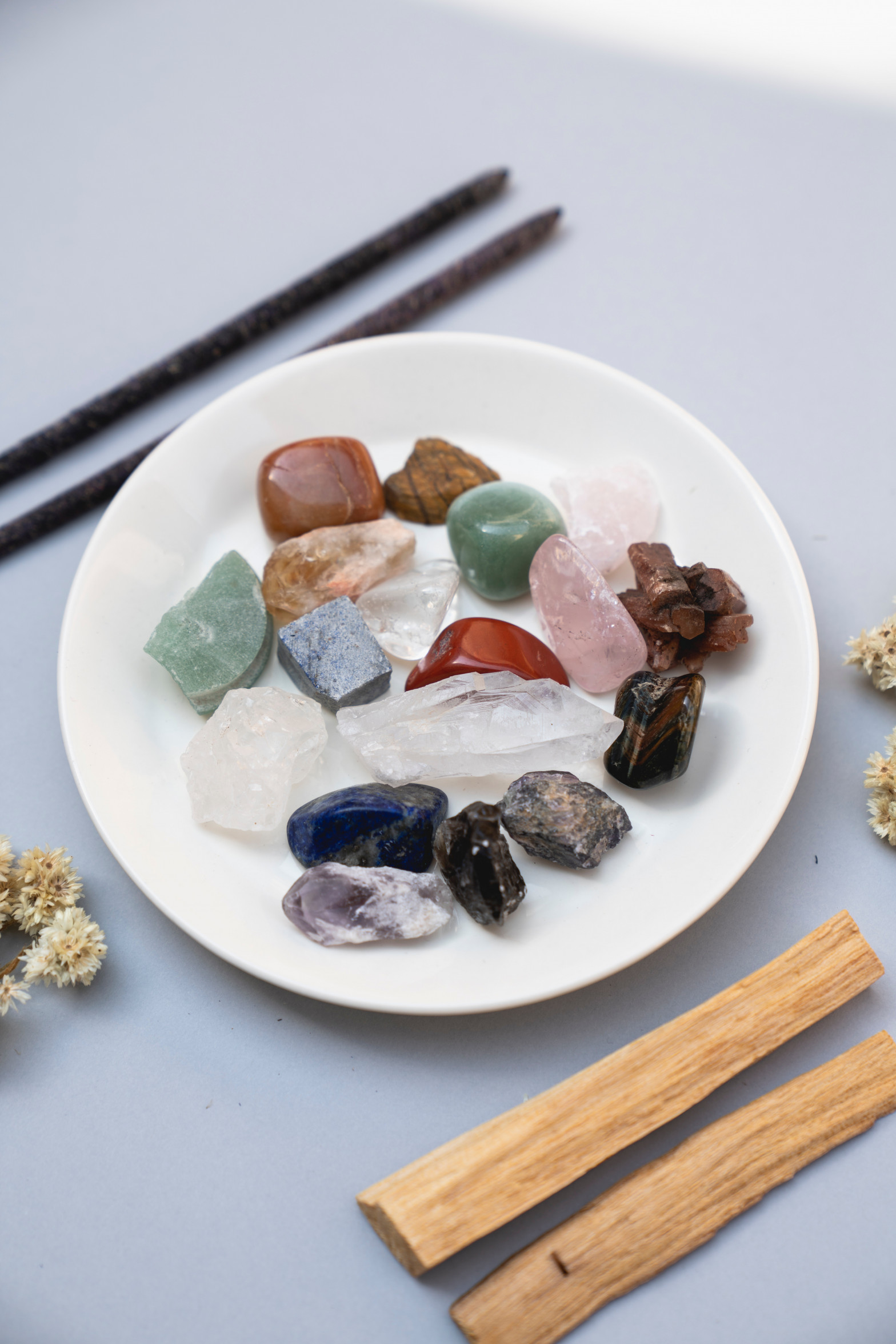 a dish filled with various crystals, with incense sitting next to it.